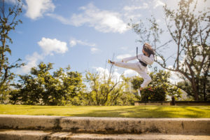 Girl doing a karate kick in front of trees in a park